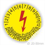 E-Check Prüfplaketten rund, Farbe- Gelb, ein Elektro- Pfeil in Rot, Startjahr- 26, Monatszahlen Oben und Jahreszahlen Unten in Kreisform. Über den Jahreszahlen Text "Nächster Prüftermin"