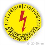 Prüfplaketten rund, Farbe- Gelb, ein Elektro- Pfeil in Rot, Startjahr- 27, Monatszahlen Oben und Jahreszahlen Unten in Kreisform. Über den Jahreszahlen Text "Nächster Prüftermin"