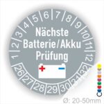 Prüfetiketten, Prüfplakette rund, Farbe- Grau, Text "Nächste Batterie/Akku Prüfung" in Weiß. Icon Batterie, Startjahr- 25, Monatszahlen Oben und Jahreszahlen Unten in Kreisform.
