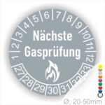 Mehrjahresplaketten, Prüfplaketten rund, Farbe- Grau, Text "Nächste Gasprüfung" in Weiß danach eine Flamme als Pictogramm oder Icon in Weiß, Startjahr- 27, Monatszahlen Oben und Jahreszahlen Unten in Kreisform.