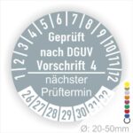 Prüfplakette mit Text Geprüft nach Dguv Vorschrift 4 und Nächster Prüftermin mit zwischen Strich in Weiss. Plaketten Farbe- Grau und Text in Weiss. Monatszahlen oben und Jahreszahlen unten beginnend mit Startjahr- 26