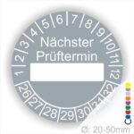 Prüfplakette, Prüfetikett rund, Farbe- Grau, Text "Nächster Prüftermin" in Weiß. Als nächstes kommt ein Beschriftungfeld / Leerfeld in Farbe Weiß. Startjahr- 26, Monatszahlen Oben und Jahreszahlen Unten in Kreisform.