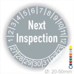 Prüfetiketten, Prüfaukleber rund, Farbe- Grau, Text auf Englisch "Next Inspection" in Weiß. Startjahr- 27, Monatszahlen Oben und Jahreszahlen Unten in Kreisform.