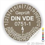 Prüfplaketten rund, Farbe- Braun, Text "Geprüft gemäß DIN VDE 0751-1" in Weiß danach ein Elektro- Pfeil in Weiß, Startjahr- 26, Monatszahlen Oben und Jahreszahlen Unten in Kreisform. Über den Jahreszahlen Text "Nächster Prüftermin"