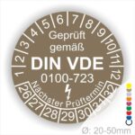 Prüfetiketten rund, Farbe- Braun, Text "Geprüft gemäß VDE 0100-0723" in Weiß danach ein Elektro- Pfeil in Weiß, Startjahr- 26, Monatszahlen Oben und Jahreszahlen Unten in Kreisform. Über den Jahreszahlen Text "Nächster Prüftermin"