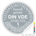 Prüfetiketten rund, Farbe- Grau, Text "Geprüft gemäß VDE 0100-0723" in Weiß danach ein Elektro- Pfeil in Weiß, Startjahr- 26, Monatszahlen Oben und Jahreszahlen Unten in Kreisform. Über den Jahreszahlen Text "Nächster Prüftermin"