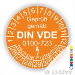 Prüfetiketten rund, Farbe- Orange, Text "Geprüft gemäß VDE 0100-0723" in Weiß danach ein Elektro- Pfeil in Weiß, Startjahr- 26, Monatszahlen Oben und Jahreszahlen Unten in Kreisform. Über den Jahreszahlen Text "Nächster Prüftermin"