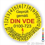 Prüfaufkleber rund, Farbe- Gelb, Text "Geprüft gemäß VDE 0100-723" in Schwarz danach ein Elektro- Pfeil in Rot, Startjahr- 27, Monatszahlen Oben und Jahreszahlen Unten in Kreisform. Über den Jahreszahlen Text "Nächster Prüftermin"