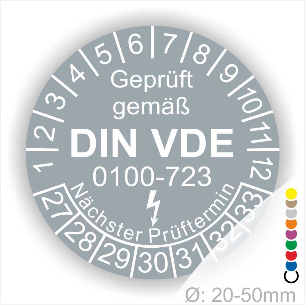 Prüfaufkleber rund, Farbe- Grau, Text "Geprüft gemäß VDE 0100-0723" in Weiß danach ein Elektro- Pfeil in Weiß, Startjahr- 27, Monatszahlen Oben und Jahreszahlen Unten in Kreisform. Über den Jahreszahlen Text "Nächster Prüftermin"
