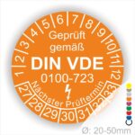Prüfaufkleber rund, Farbe- Orange, Text "Geprüft gemäß VDE 0100-0723" in Weiß danach ein Elektro- Pfeil in Weiß, Startjahr- 27, Monatszahlen Oben und Jahreszahlen Unten in Kreisform. Über den Jahreszahlen Text "Nächster Prüftermin"
