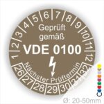 Prüfplaketten rund Farbe- Braun, Text "Geprüft gemäß VDE 0100" in Weiß danach ein Elektro- Pfeil in Weiß, Startjahr- 26, Monatszahlen Oben und Jahreszahlen Unten in Kreisform. Über den Jahreszahlen Text "Nächster Prüftermin"