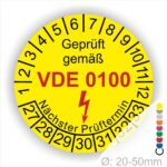 Prüfaufkleber rund, Farbe- Gelb, Text "Geprüft gemäß VDE 0100" in Schwarz danach ein Elektro- Pfeil in Rot, Startjahr- 27, Monatszahlen Oben und Jahreszahlen Unten in Kreisform. Über den Jahreszahlen Text "Nächster Prüftermin"