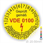 Prüfaufkleber rund, Farbe- Gelb, Text "Geprüft gemäß VDE 0100" in Schwarz danach ein Elektro- Pfeil in Rot, Startjahr- 28, Monatszahlen Oben und Jahreszahlen Unten in Kreisform. Über den Jahreszahlen Text "Nächster Prüftermin"