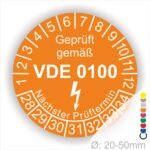 Prüfetikette rund, Farbe- Orange, Text "Geprüft gemäß VDE 0100" in Weiß danach ein Elektro- Pfeil in Weiß, Startjahr- 28, Monatszahlen Oben und Jahreszahlen Unten in Kreisform. Über den Jahreszahlen Text "Nächster Prüftermin"