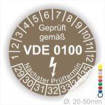 Prüfetikette rund, Farbe- Braun, Text "Geprüft gemäß VDE 0100" in Weiß danach ein Elektro- Pfeil in Weiß, Startjahr- 29, Monatszahlen Oben und Jahreszahlen Unten in Kreisform. Über den Jahreszahlen Text "Nächster Prüftermin"
