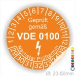 Prüfetikette rund, Farbe- Orange, Text "Geprüft gemäß VDE 0100" in Weiß danach ein Elektro- Pfeil in Weiß, Startjahr- 29, Monatszahlen Oben und Jahreszahlen Unten in Kreisform. Über den Jahreszahlen Text "Nächster Prüftermin"