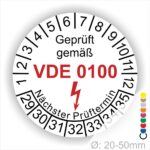 Prüfaufkleber, Prüfsiegel rund, Farbe- Weiß, Text "Geprüft gemäß VDE 0100" in Schwarz danach ein Elektro- Pfeil in Rot, Startjahr- 29, Monatszahlen Oben und Jahreszahlen Unten in Kreisform. Über den Jahreszahlen Text "Nächster Prüftermin"