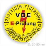 Prüfplaketten rund, Farbe- Gelb, Text "VDE E-Prüfung" in Schwarz in Hinergrund ein Elektro- Pfeil in Rot, Startjahr- 28, Monatszahlen Oben und Jahreszahlen Unten in Kreisform. Über den Jahreszahlen Text "Nächster Prüftermin"