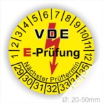 Prüfplaketten rund, Farbe- Gelb, Text "VDE E-Prüfung" in Schwarz in Hinergrund ein Elektro- Pfeil in Rot, Startjahr- 29, Monatszahlen Oben und Jahreszahlen Unten in Kreisform. Über den Jahreszahlen Text "Nächster Prüftermin"