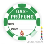 Grünes Aufkleber-Design für Gasprüfungen mit Platz für Name und Datum, Durchmesser 30-50 mm, enthält ein feuerförmiges Symbol. Ideal für Sicherheitskennzeichnungen in der Gasinstallation.