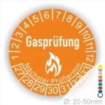 Gasprüfungs-Plakette in orange mit der Aufschrift "Gasprüfung" und dem Hinweis "Nächster Prüftermin" sowie einem Flammensymbol. Die Plakette zeigt eine Skala von 1 bis 12 und 27 bis 33 zur Kennzeichnung des Prüfzeitraums. Durchmesser 20-50 mm.