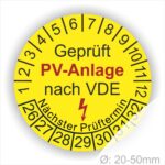 Prüfplaketten rund, Farbe- Gelb, Text "Geprüft PV-Anlage nach VDE" in Schwarz danach ein Elektro- Pfeil in Rot, Startjahr- 26, Monatszahlen Oben und Jahreszahlen Unten in Kreisform. Über den Jahreszahlen Text "Nächster Prüftermin"